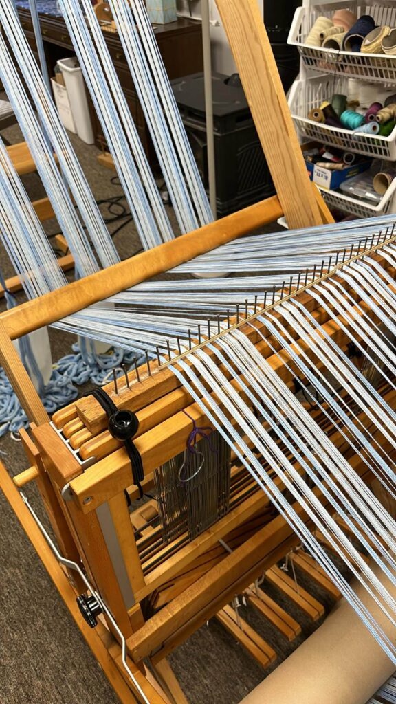 The warp is routed under the front beam and through the raddle, that is located on top of the loom castle.