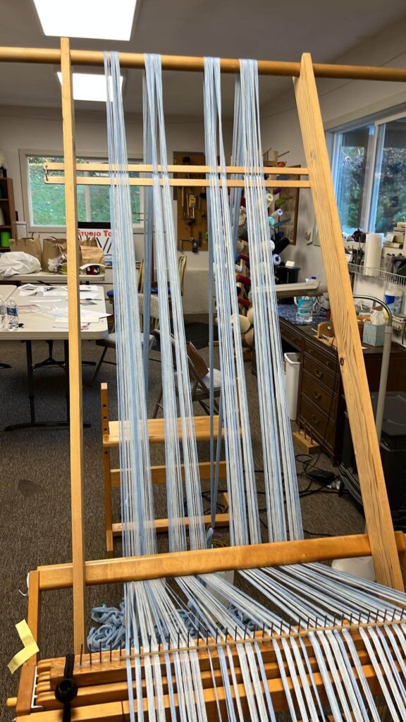 The warp goes from the floor over the dowel, then under the front beam of the loom.