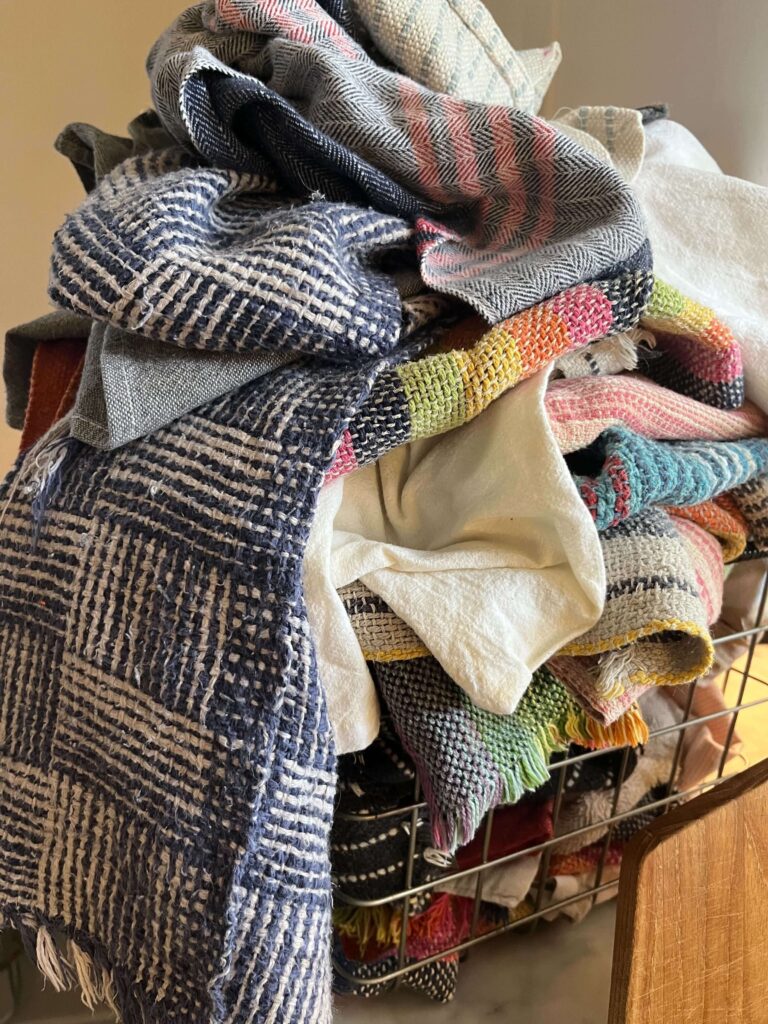 A pile of multicolored handwoven fabrics overflowing a basket