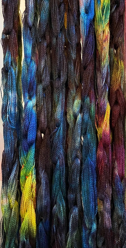 warp chains that have dried, hanging vertically. They are a random mix of shades of blue, purple, black, yellow, lime green, and some deep rusty red
